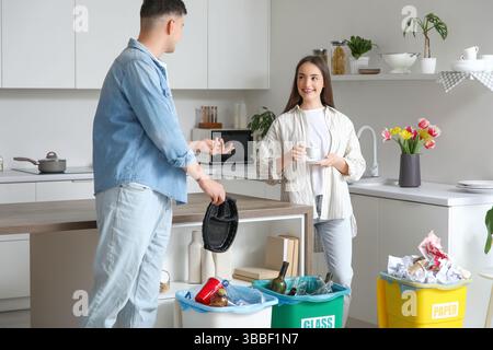 Young couple sorting rubbish in garbage bins at home. Global Recycling Day Stock Photo