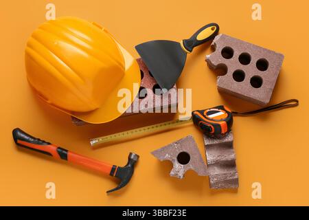 Hardhat, bricks and construction tools on orange background Stock Photo