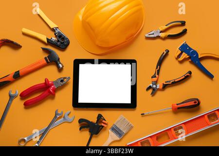 Tablet computer with blank screen, hardhat and construction tools on orange background Stock Photo
