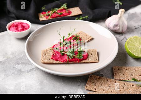 Plate with crispbreads, tasty beetroot hummus and microgreen on grunge background Stock Photo