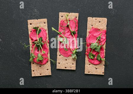 Crispbreads with tasty beetroot hummus and sprouts on dark background Stock Photo