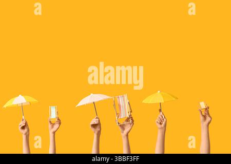 Female hands holding mini deck chairs with umbrellas on yellow background Stock Photo
