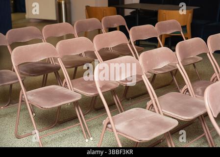 Neatly arranged pink velvet folding chairs set up in a meeting or event space, ready for attendees or audience seating. Stock Photo