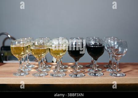 Rows of wine glasses filled with red and white wine arranged on a wooden counter, ready for serving at a celebration. Stock Photo