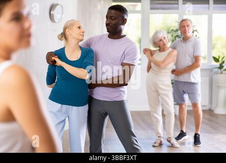 Young woman teaching group of multiethnic mature people social dance Stock Photo