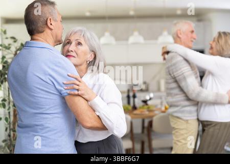Two married couples enjoying slow dancing at house party for friends Stock Photo