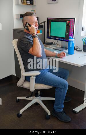 Man sitting at desk talking on smartphone, work from home lifestyle Stock Photo
