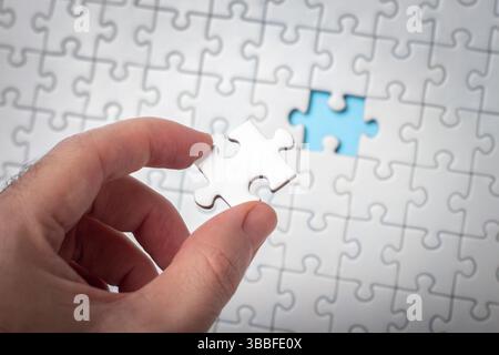 Hand Holding Puzzle Piece with Incomplete Puzzle Background Stock Photo