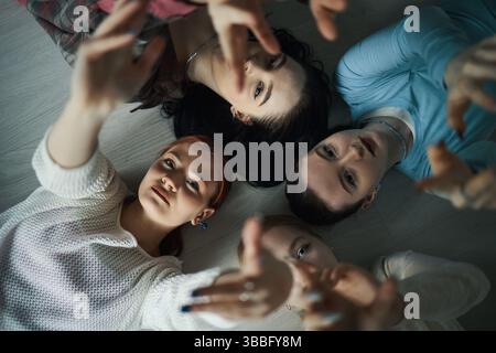 Teenagers Lying on Floor With Hands Reaching Upward Stock Photo
