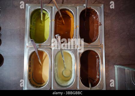 Top view of six metal containers filled with various ice cream flavors, each a different color. Ladles are placed in each container for serving differ Stock Photo
