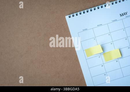 Calendar page with yellow adhesive notes. On top of brown cardboard surface, high angle view. Copy space. Stock Photo