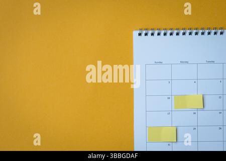 Calendar page with yellow adhesive notes. On top of yellow surface, high angle view. Copy space. Stock Photo