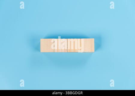 Four wooden blocks arranged in a straight horizontal line on blue background, symbolizing foundation, alignment, stability. Minimal and clean concept Stock Photo
