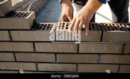 Construction worker carefully placing bricks and applying mortar, skillfully building a sturdy new wall on a bustling construction site Stock Photo