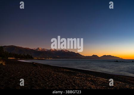 Orange light on the snowy mountains before sunrise at Kaikoura beach, South Island, New Zealand Stock Photo