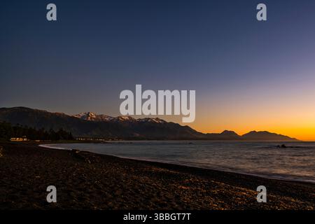 Light on the snowy mountains just before sunrise at Kaikoura beach, South Island, New Zealand Stock Photo