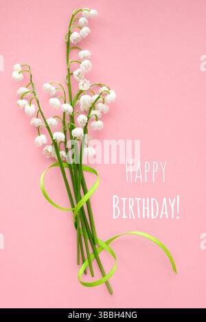 Lily of the valley bouquet tied with a green ribbon placed on a pink background. Includes the text "Happy Birthday" in white, creating a festive greet Stock Photo