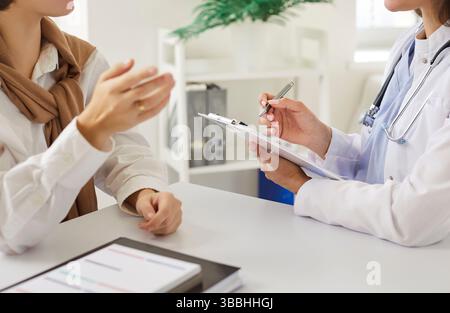 Female doctor attentively listening to patient, taking notes during consultation in medical office. Stock Photo
