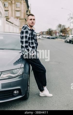 Young man in plaid shirt leaning on a car outdoors Stock Photo