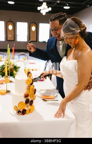 Bride and groom smile while cutting white and orange wedding cake Stock Photo