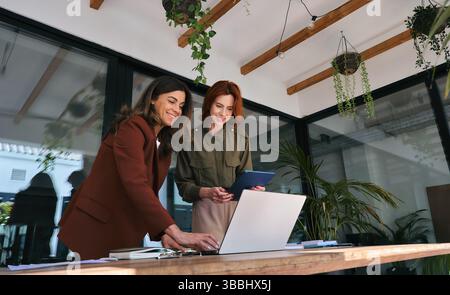 Two happy busy business women talking working in green cozy office. Stock Photo