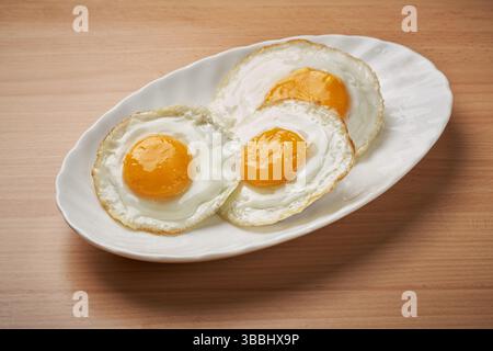 Three fried eggs arranged on a plate on a wooden table Stock Photo