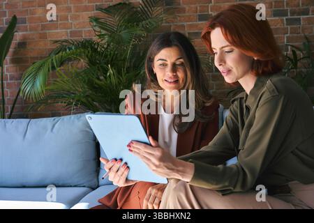Two busy happy business women talking using tab working sitting in office. Stock Photo
