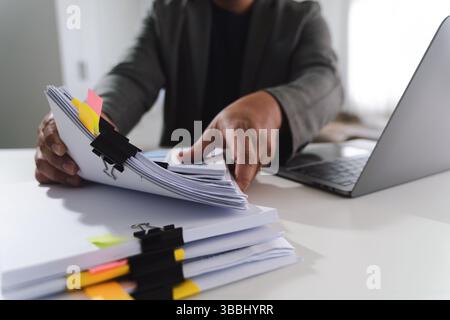 A pen signing a document person organizing documents with laptop desk, showing busy workspace and paperwork management, conveying productivity Stock Photo