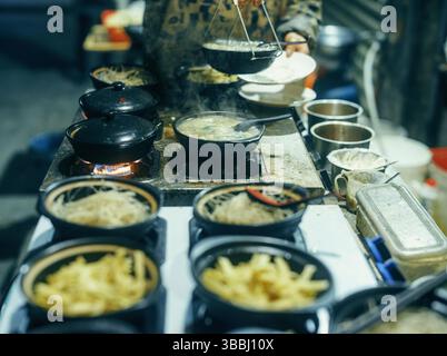 Clay Pot Noodle Bowls Simmering on Gas Burners at a Wuhan Night Market Snack Stall, Hubei, China Stock Photo