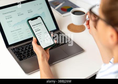 Woman managing finances via online banking app at home using laptop and smartphone Stock Photo