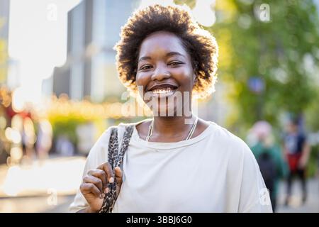 Portrait of a smiling young woman standing in the city on a sunny day Stock Photo