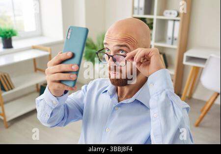 Funny young businessman using smart phone watching screen, smiling office professional smartphone  Stock Photo