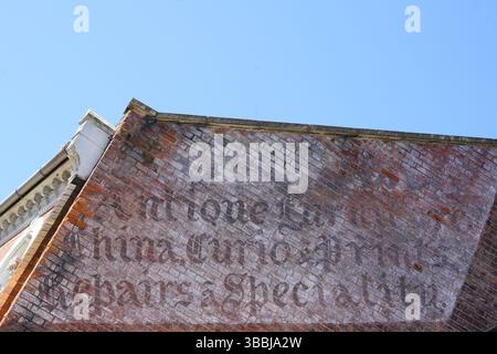 Historic Brick Wall with Faded Signage Against Clear Blue Sky. Dorking, UK Stock Photo