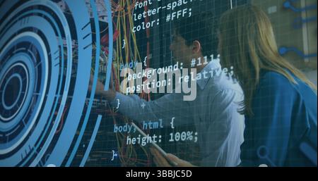 Collaborating IT technicians adjusting network cables in server rack, with tablet and code overlays Stock Photo