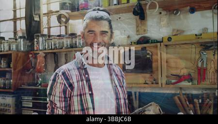 Reviewing woodworking project, man with ponytail holding tablet in workshop, with jars and clamps Stock Photo