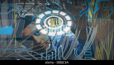 Hispanic man threading network cables in server room, with patch panels and holographic interface Stock Photo