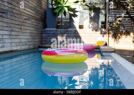 Yellow and pink inflatable ring floating in backyard pool with donut float, beach ball, planters Stock Photo