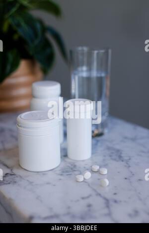 Medication bottles are standing on marble countertop, tablets lying near water glass and plant Stock Photo
