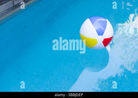 Multicolored inflatable beach ball is floating on clear blue pool water and creating reflections Stock Photo