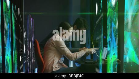 Image of shapes over diverse man and woman working on laptop in server room Stock Photo