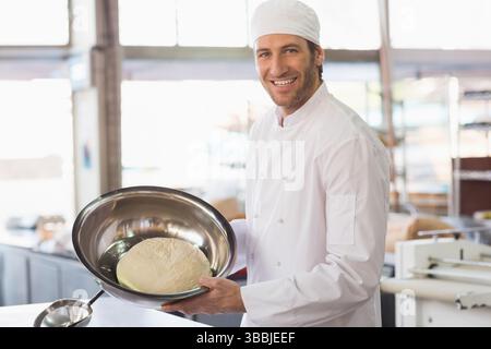 Holding dough in stainless steel bowl, male chef working at counter in bakery kitchen, copy space Stock Photo