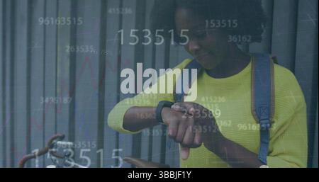 Multiple changing numbers floating over african american woman using smartwatch on the street Stock Photo