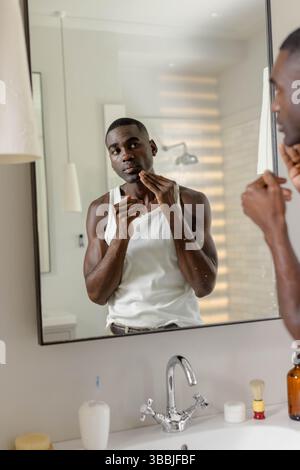 African American man touching chin while inspecting skin at bathroom vanity, with amber bottle Stock Photo