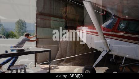 Pushing man in jeans opening hangar door at hangar entrance, with propeller plane, piano overlay Stock Photo