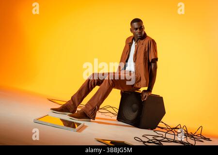 African American man sitting on speaker in studio, with reflective panels, audio cables, copy space Stock Photo