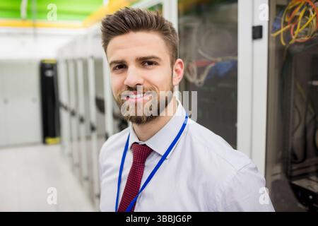 Smiling man standing inside data center, with server racks, network cables and ID badge Stock Photo