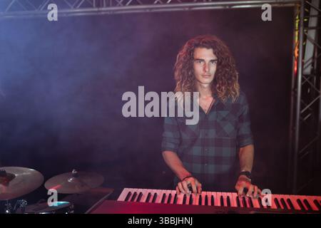 Red keyboard is resting beside drum cymbals on dark stage, illuminated by colored spotlights Stock Photo