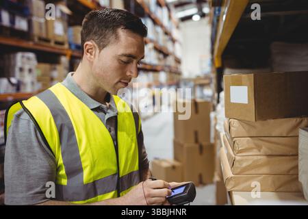 Scanning man using handheld barcode scanner in warehouse aisle, with cardboard boxes, copy space Stock Photo
