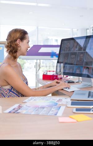 Computer monitor is displaying grid of profile photos on wooden desk in modern office, with laptop Stock Photo