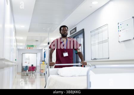 African American male hospital worker pushing bed in hospital corridor, with IV pole and ID badge Stock Photo